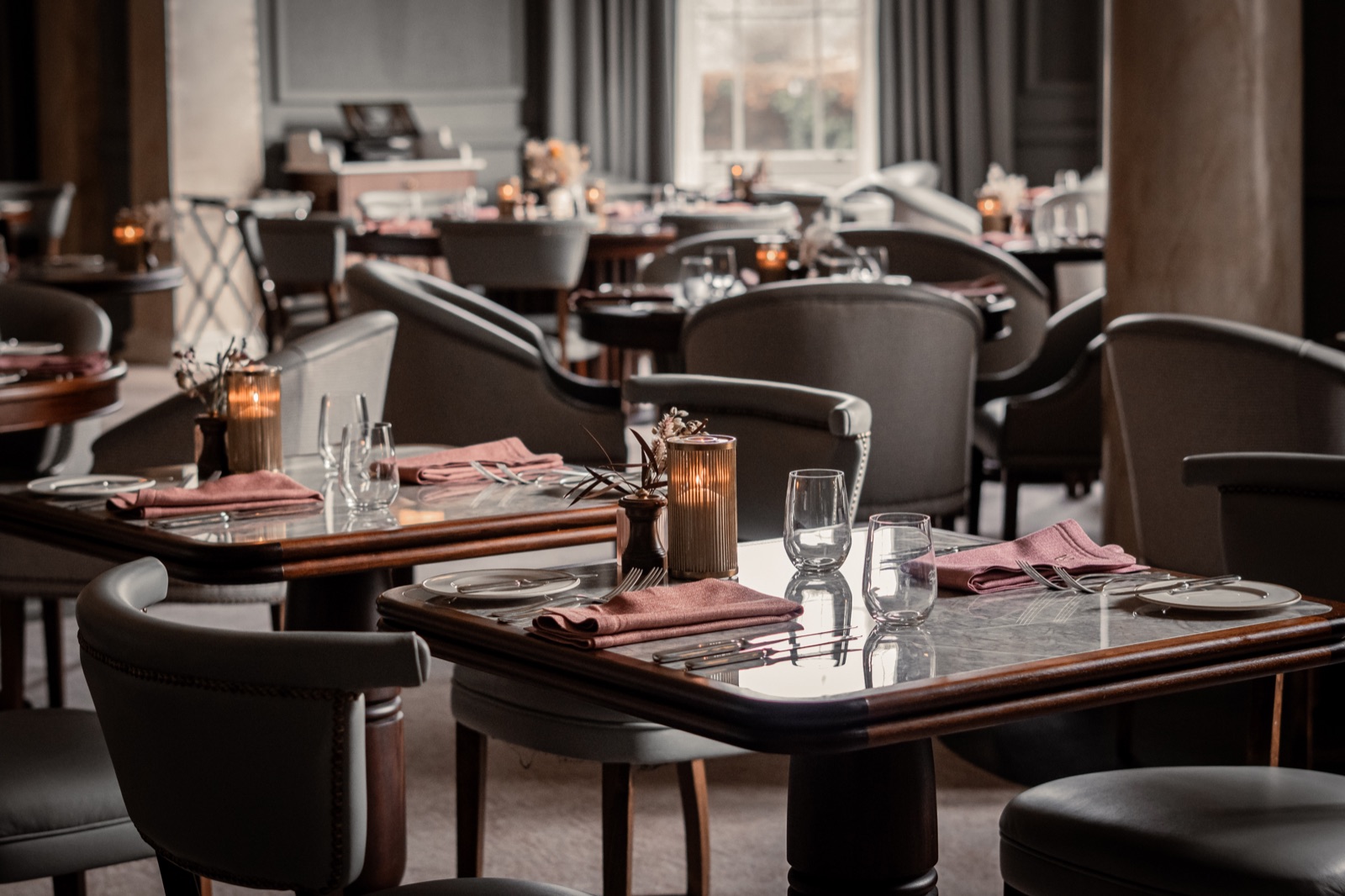 Elegant dining room with upholstered chairs, set tables and warm candlelight.